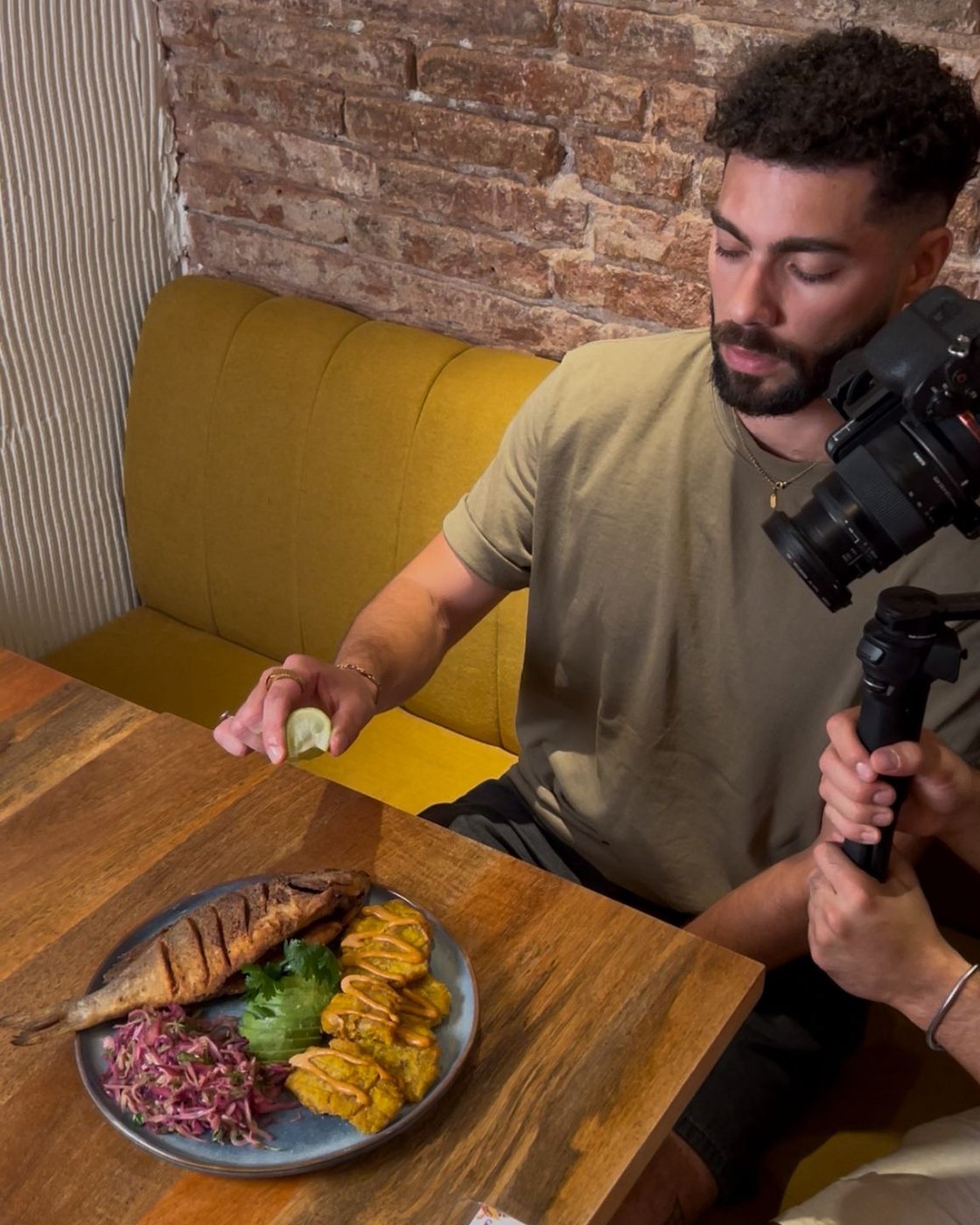 Eithan squeezing lime over fried fish and patacones during a content shoot at La Churuata